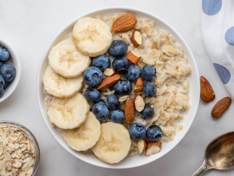 Eine Schüssel Soja-Porridge mit Bananen, Blaubeeren und Mandeln in der Draufsicht.