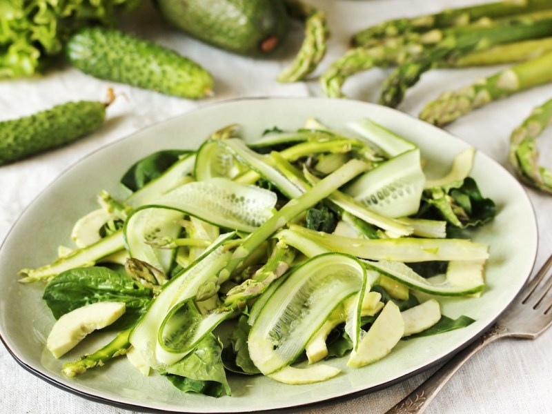 Ein Teller Spargel-Gurken-Salat, drumherum kleine Gurken und grüner Spargel.