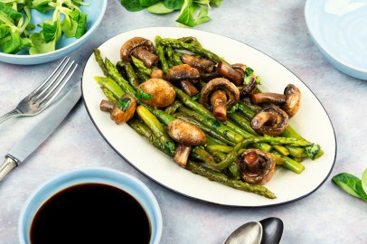 Spargel-Pilz-Pfanne auf einem ovalen Teller, daneben Besteck und eine Schale Feldsalat.