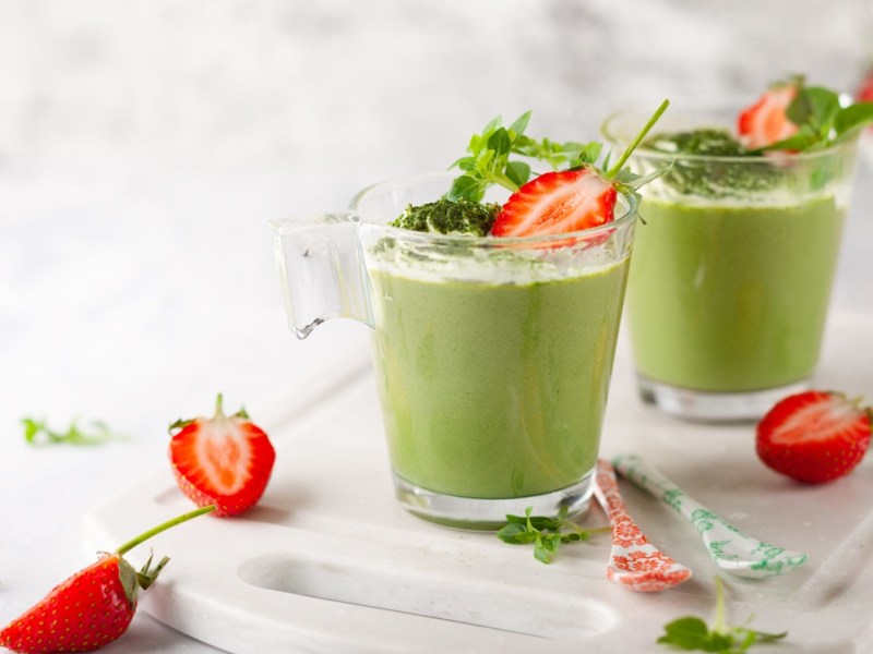 Zwei Gläser mit Waldmeister-Mousse, garniert mit frischen Erdbeeren.