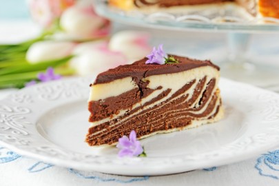 Ein Stück Zebra-Käsekuchen mit hellem und dunklem Teig auf einem Teller, dekoriert mit Blüten.
