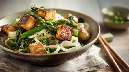 Eine Schüssel Zitronenspargel mit Reisnudeln und gebratenem Tofu. Daneben Essstäbchen. Nahausnahme.