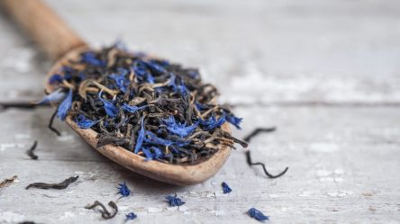 Earl Grey selbst machen: Ein Löffel Earl Grey mit Kornblumenblüten liegt auf einem hellen Holztisch.