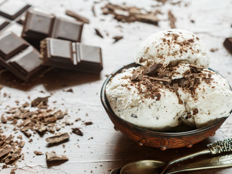 3 Kugeln Eierlikör-Eis mit Schokolade in einer Schüssel, drumherum Schokolade.