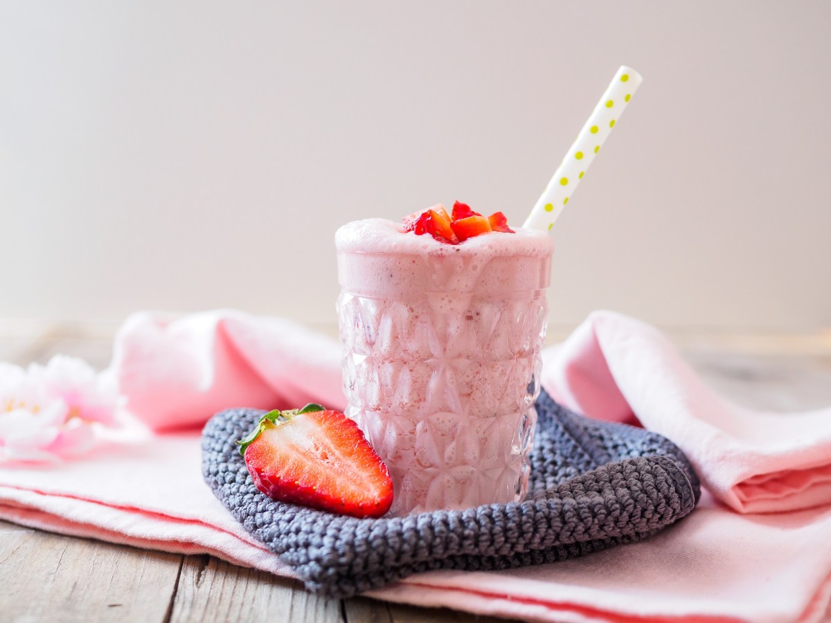 Glas Erdbeer-Buttermilch-Smoothie auf einem Küchentuch stehend mit Strohhalm im Glas