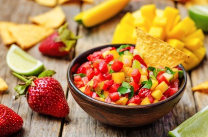 Eine Schale Erdbeer-Mango-Salsa mit einem Nacho, drumherum Erdbeeren, Mango und Limettenspalten.
