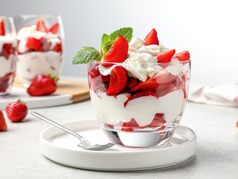 Erdbeer-Mascarpone-Schichtdessert im Glas, im Hintergrund weitere Gläser mit dem Nachtisch sowie frische Erdbeeren.