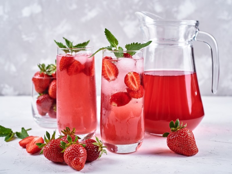 2 Gläser Erdbeerlimonade mit Mango und Banane, daneben ein Krug mit der Limo und einige frische Erdbeeren.