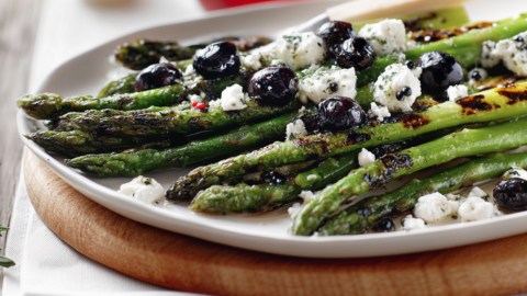 Gegrillter Spargel mit Ziegenkäse und Oliven auf einem Teller.