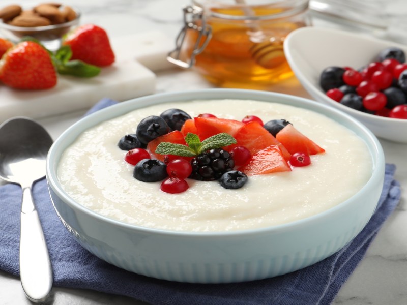 Eine Schüssel Grießbrei mit Eierlikör und Beeren, daneben ein Löffel und ein paar Zutaten.