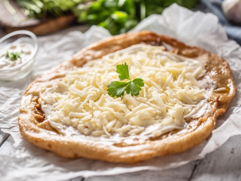 Ein Langos aus der Heißluftfritteuse mit Knoblauchcreme und geriebenem Käse.