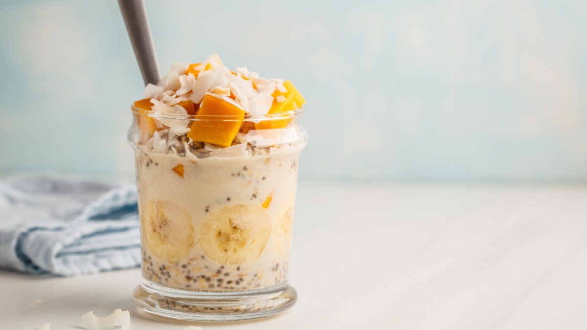 Mango-Kokos-Overnight-Oats im Glas geschichtet und serviert mit einem Strohhalm.
