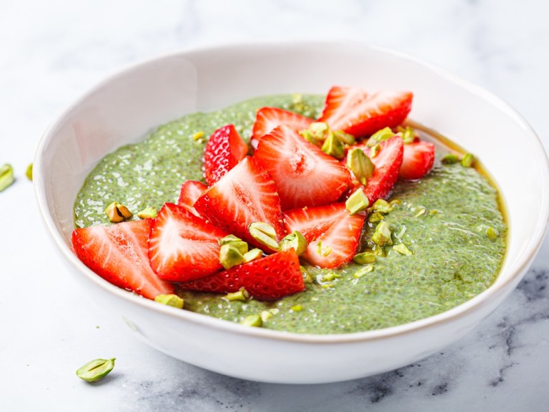 Matcha-Erdbeer-Chiapudding, garniert mit gehackten Pistazien, in einer weißen Schüssel.