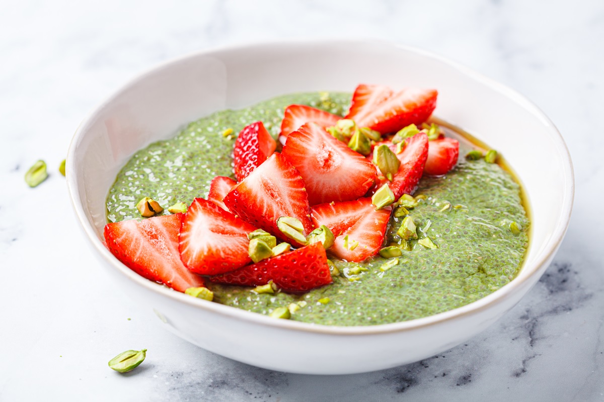 Matcha-Erdbeer-Chiapudding, garniert mit gehackten Pistazien, in einer weißen Schüssel.