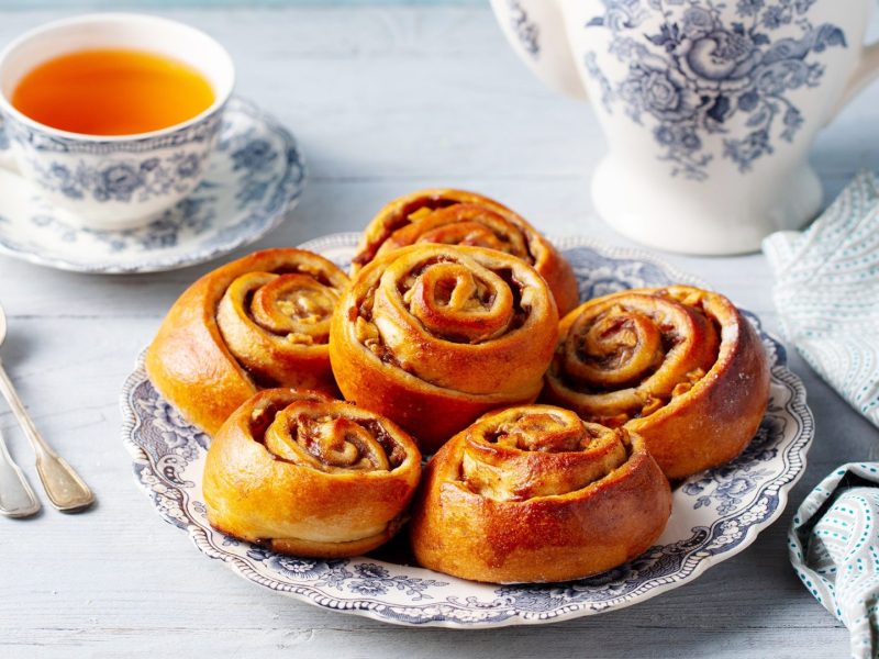 Nussschnecken auf einem gemusterten Teller. Dahinter eine Tasse Tee.