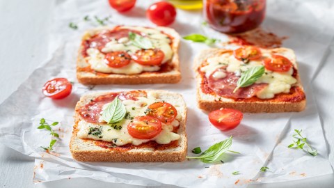 3 Pizza-Toasts aus dem Airfryer auf einem Stück Backpapier, belegt mit Käse, Tomaten und Salami.