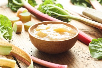 Eine Schale Rhabarbergrütze. Daneben liegen frische Rhabarberstangen.