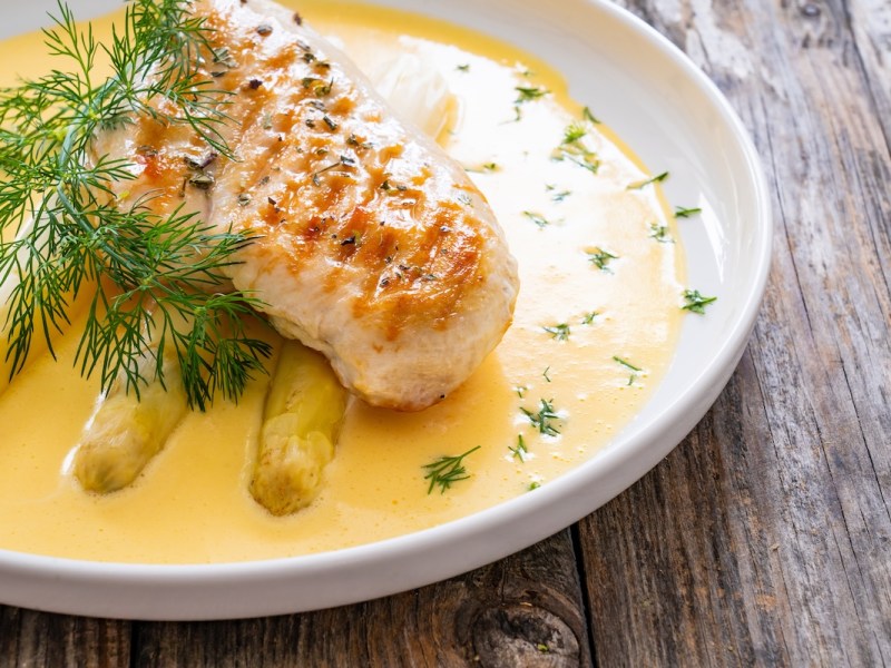Ein Teller Spargel mit Miso-Hollandaise und einem Stück Hähnchenbrust. Nahaufnahme.