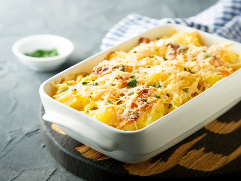 Überbackener Kohlrabi in weißer Auflaufform, die auf enem Brett steht.