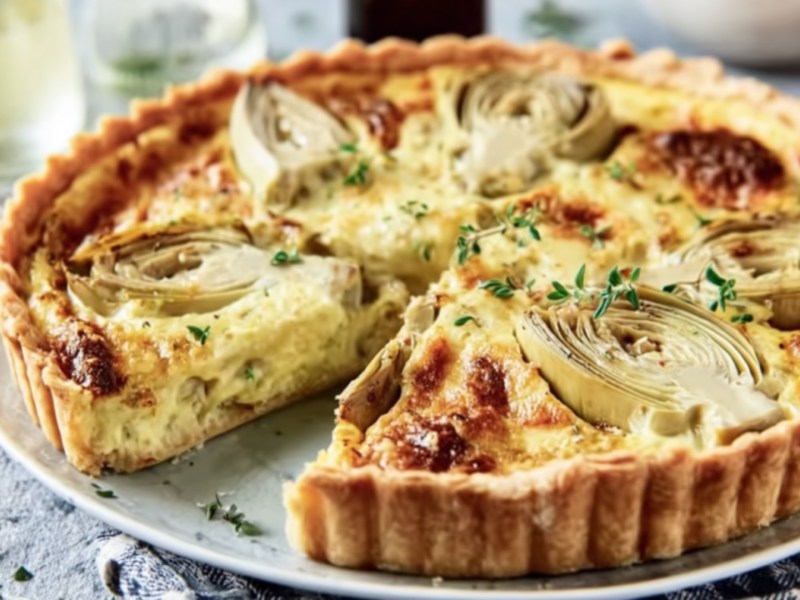 Eine Artischocke.Quiche auf einem Teller, aus der ein Stück herausgeschnitten wurde.