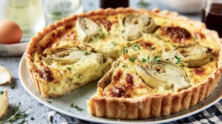 Eine Artischocke.Quiche auf einem Teller, aus der ein Stück herausgeschnitten wurde.