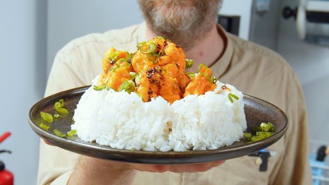 Ein Teller mit einer großen Portion Reis, auf der die Bang Bang Garnelen verteilt sind. Koch Oli hält den Teller in die Kamera.