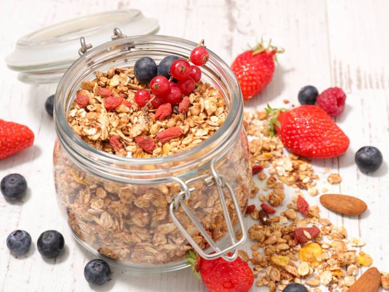 Ein Glas Beeren-Knuspermüsli, drum herum liegen frische Beeren.