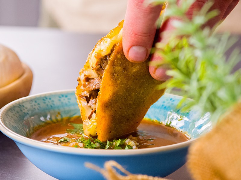 Birria-Tacco, der in Soße getunkt wird