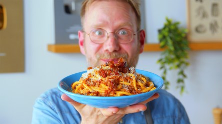 Koch Oli hält einen Teller mit Bucatini all'Amatriciana in die Kamera.
