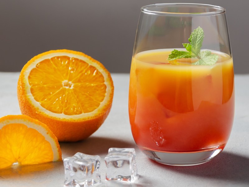 Ein Glas Campari Orange mit Minze. Daneben liegt eine halbe Orange.