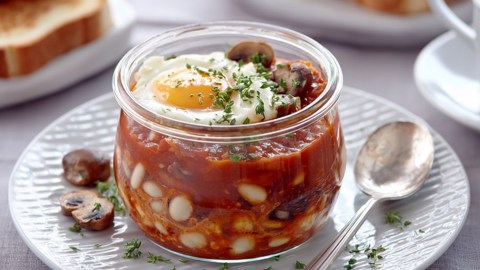 Ein englisches Frühstück im Glas auf einem Teller. Daneben liegt ein Löffel.