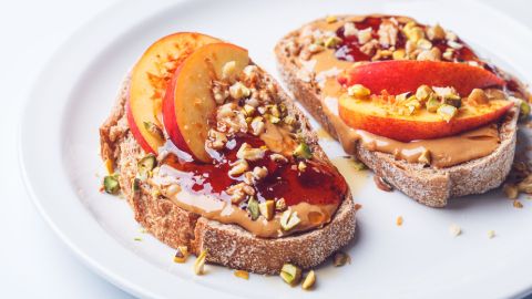 Zwei Scheiben Erdnussbutter-Pfirsich-Toast mit gehackten Nüssen und Marmelade.