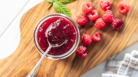Ein Glas kaltgerührte Himbeerkonfitüre im Glas in der Draufsicht. Eine Löffel mit Konfitüre befindet sich über dem Glas.