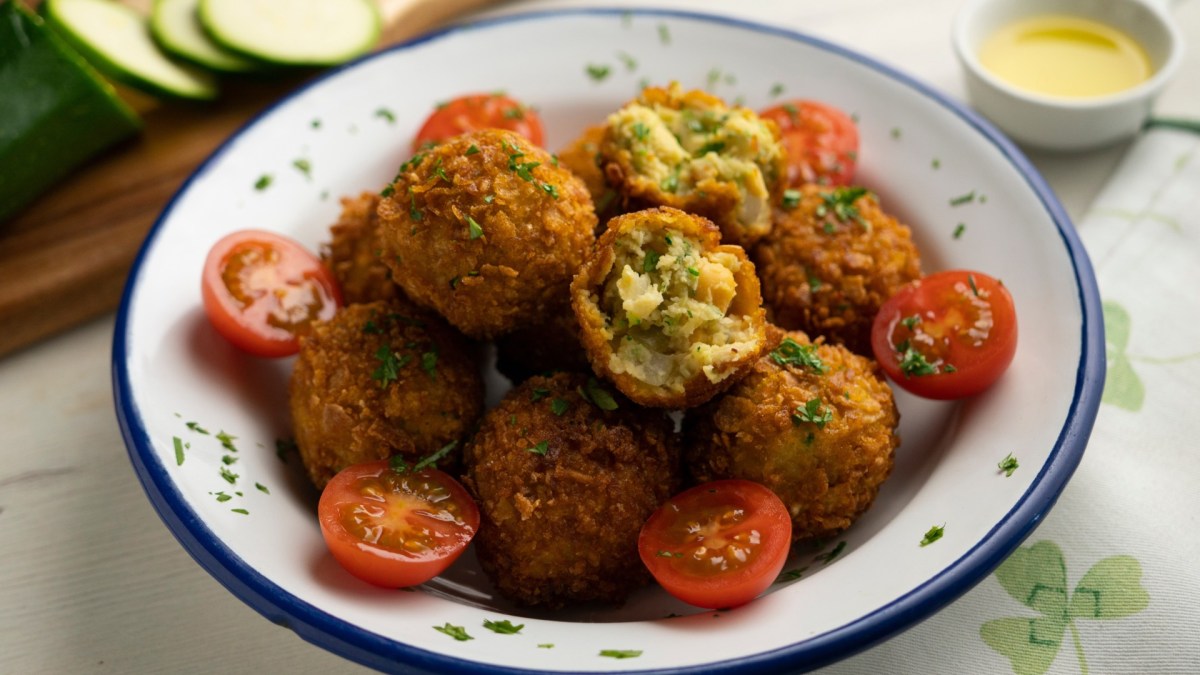 Kichererbsen-Zucchini-Kroketten auf einem tiefen Teller. Drum herum liegen Kirschtomaten.