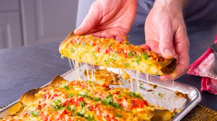 Knusprige Lasagnerollen auf einem Backblech. Eine wird hochgehoben und zieht käsige Fäden.