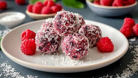 Teller mit Kokos-Himbeer-Energy-Balls und frischen Himbeeren