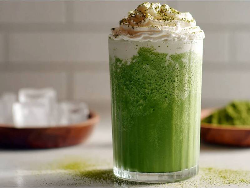 Glas Matcha Frappuccino auf einem Tisch, Schale Eiswürfel daneben