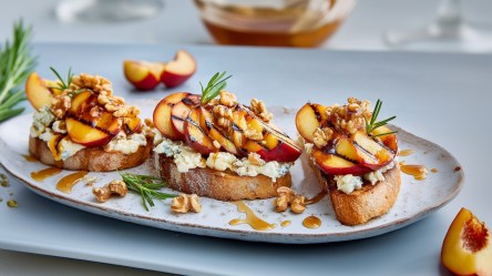 Ein Servierteller mit einigen Scheiben Nektarinen-Bruschetta. Außerdem liegen einzelne Nektarinenstücke und ein frischer Zweig Rosmarin herum.