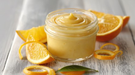 Ein Glas Orangenkaramell-Aufstrich mit frischen Orangen daneben.