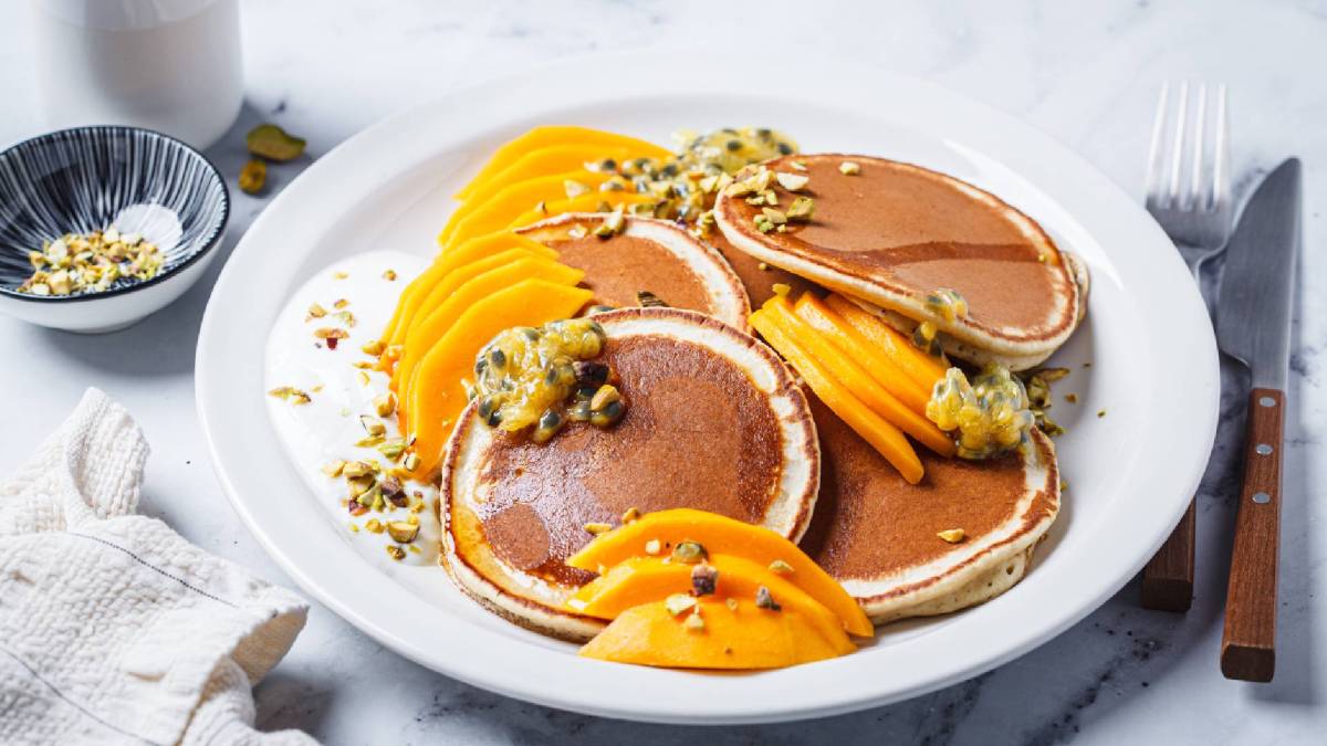 Pancakes mit Mango und Passionsfrucht auf einem weißen Teller, garniert mit gehackten Pistazien.