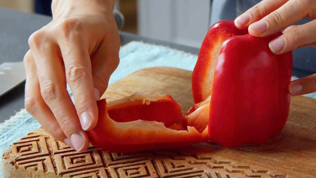 Paprika schneiden: Eine Köchin drückt eine Seite einer Paprika mit ihren Händen runter.