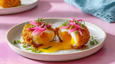 Pochierte Eier in Panko-Knusperpanade auf einem hellen Teller, garniert mit eingelegten roten Zwiebeln.