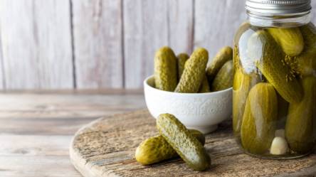 Ein Glas eingelegte Salz-Dill-Gurken neben einer Schüssel mit ebendiesen Gurken.