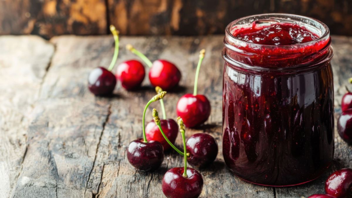 Ein Glas Sauerkirschmarmelade, im Hintergrund und daneben liegen Sauerkirschen.