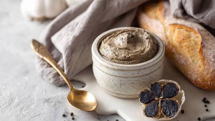 Schale mit schwarzem Knoblauch, eine aufgeschnittene Knolle und Baguette daneben