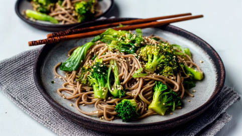 Ein Teller mit Soba-Nudeln mit Brokkoli und Pak Choi. Daneben liegen Esststäbchen.