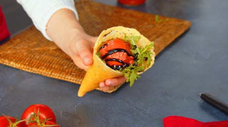 Eine Köchin hält eine Parmesanwaffel mit einer Kugel Tomatensorbet in die Kamera.