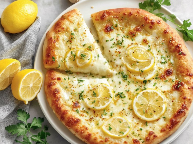 Eine Zitronen-Pizza in der Draufsicht. Daneben liegen frische Zutaten.