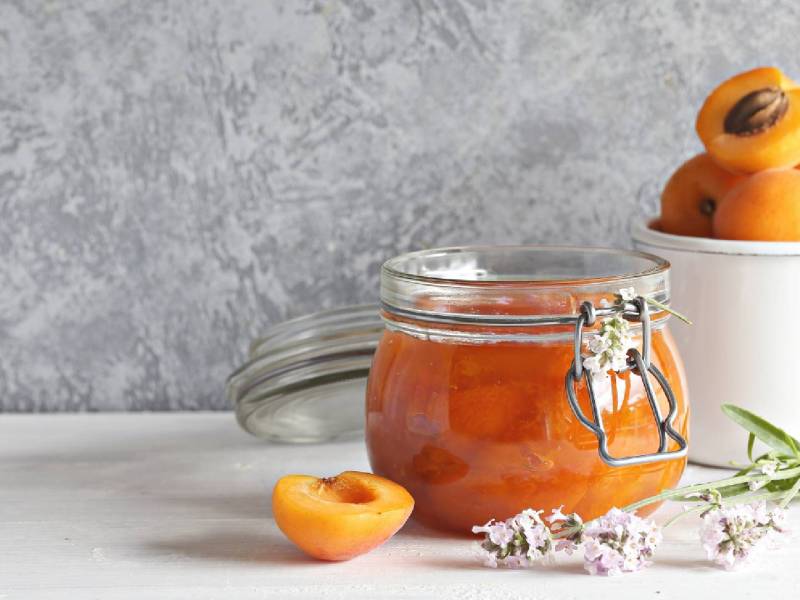 Glas Aprikosen-Lavendel-Marmelade mit frischen aprikosen daneben