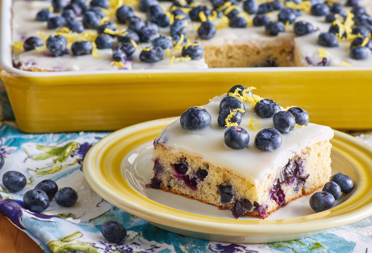 Ein Stück Blaubeer-Zitronen-Kuchen vom Blech. Im Hintergrund ist der restliche Kuchen.